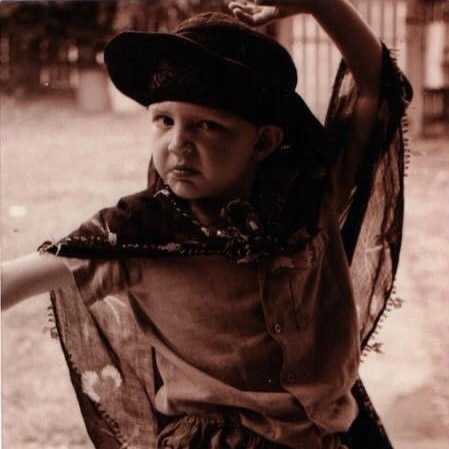A black and white photo of a young kid in a hate and scarf dancing