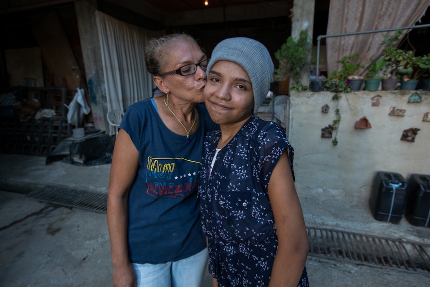 A woman kisses the cheek of a teen wearing a beanie