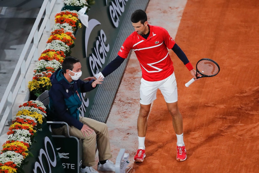A tennis player reaches out to pat a mask-wearing linesman on the shoulder at a tournament.