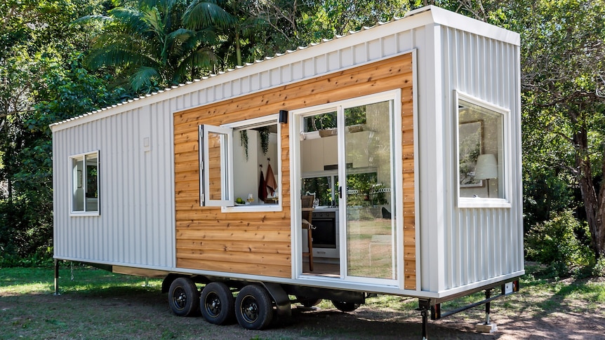 Tiny house like a shipping container with grey colourbond and timber cladding in a green garden