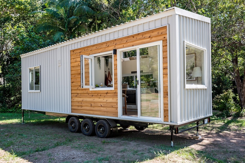 Tiny house like a shipping container with grey colourbond and timber cladding in a green garden