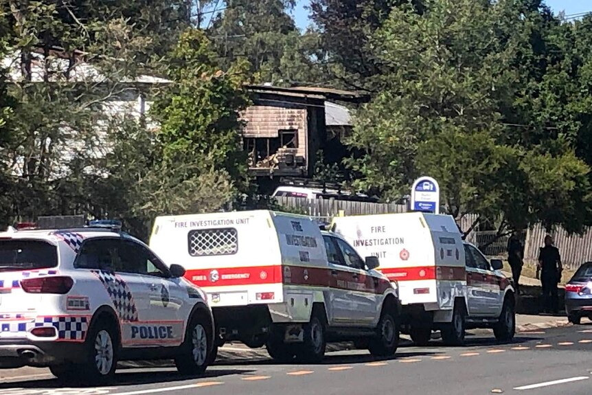 Emergency vehicles parked in a street near a house gutted by fire