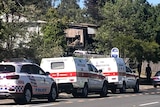 Emergency vehicles parked in a street near a house gutted by fire