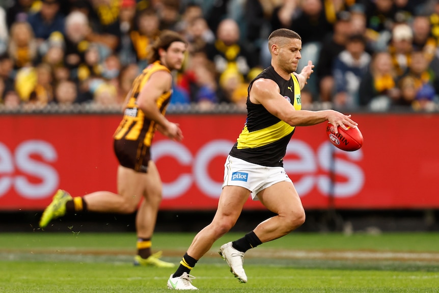 A Richmond AFL player looks down as he drops the ball onto his boot for a kick on the run.