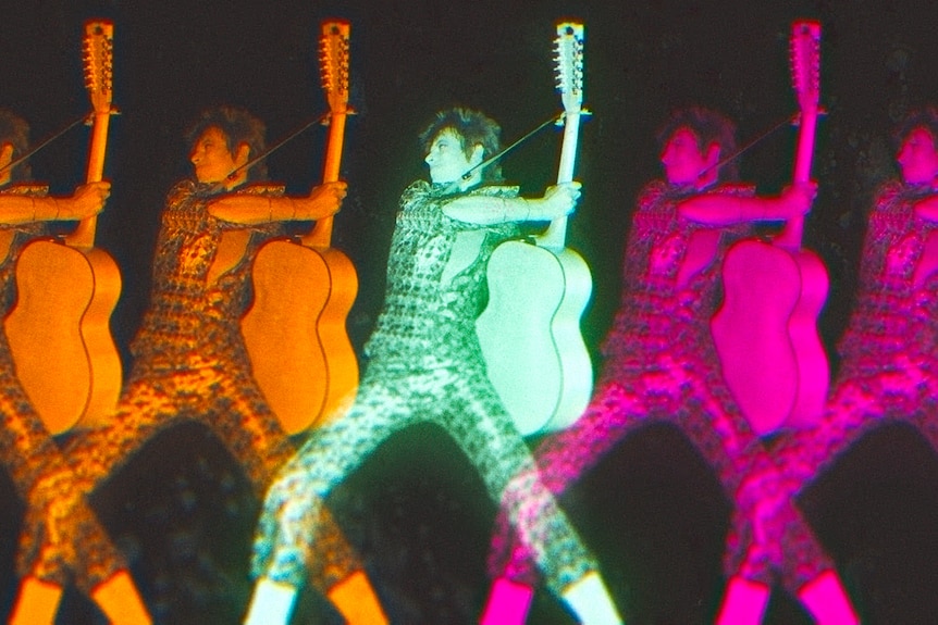 A mullet-hired David Bowie wearing a patterned jumpsuit and playing guitar is duplicated with a colourful kaleidoscopic effect.
