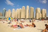 A group of people lying on a beach with a row of skyscrapers in the background