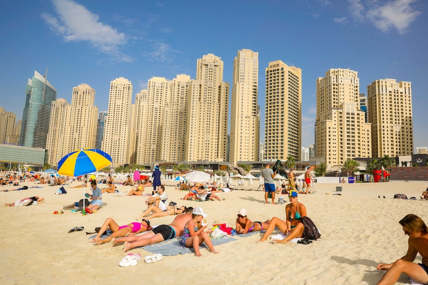 A group of people sunning themselves on a beach, with a row of skyscrapers in the background