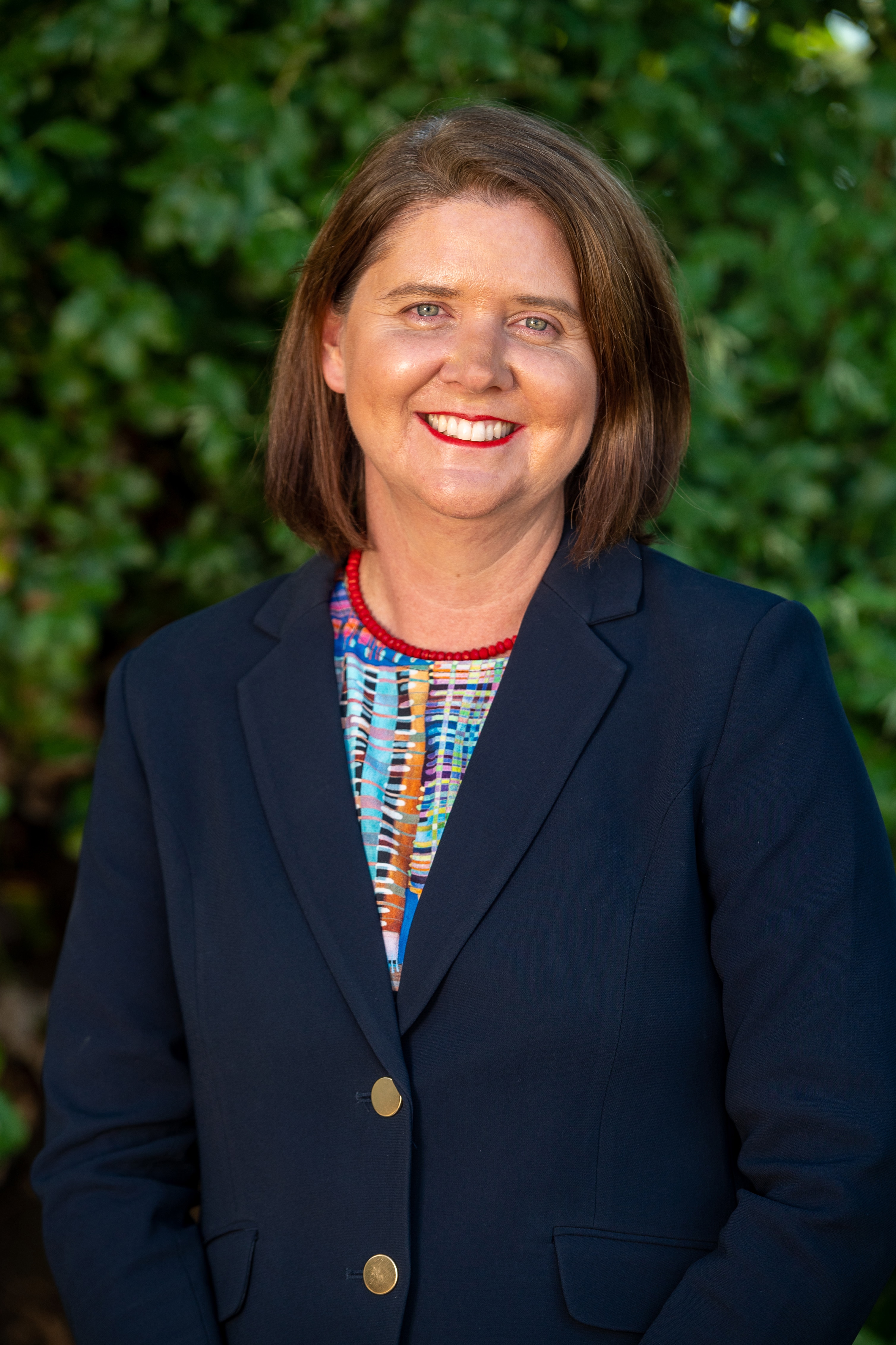 Woman in a dark suit with short hair, smiling outside.