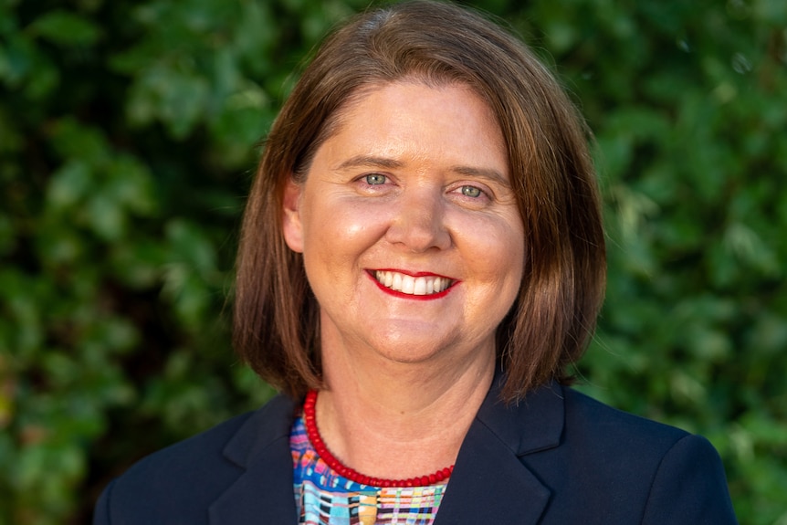 Woman in a dark suit with short hair, smiling outside.