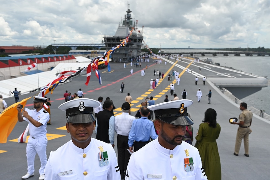 Navy officers and attendees gather on the deck of an aircraft carrier