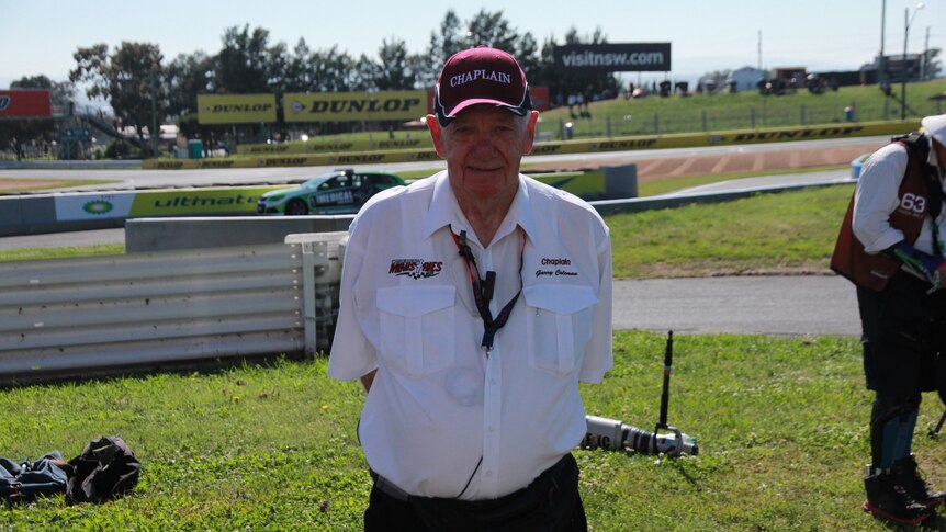 80-year old Garry Coleman wearing a white shirt and red hat in front of the final turn of Bathurst 1000