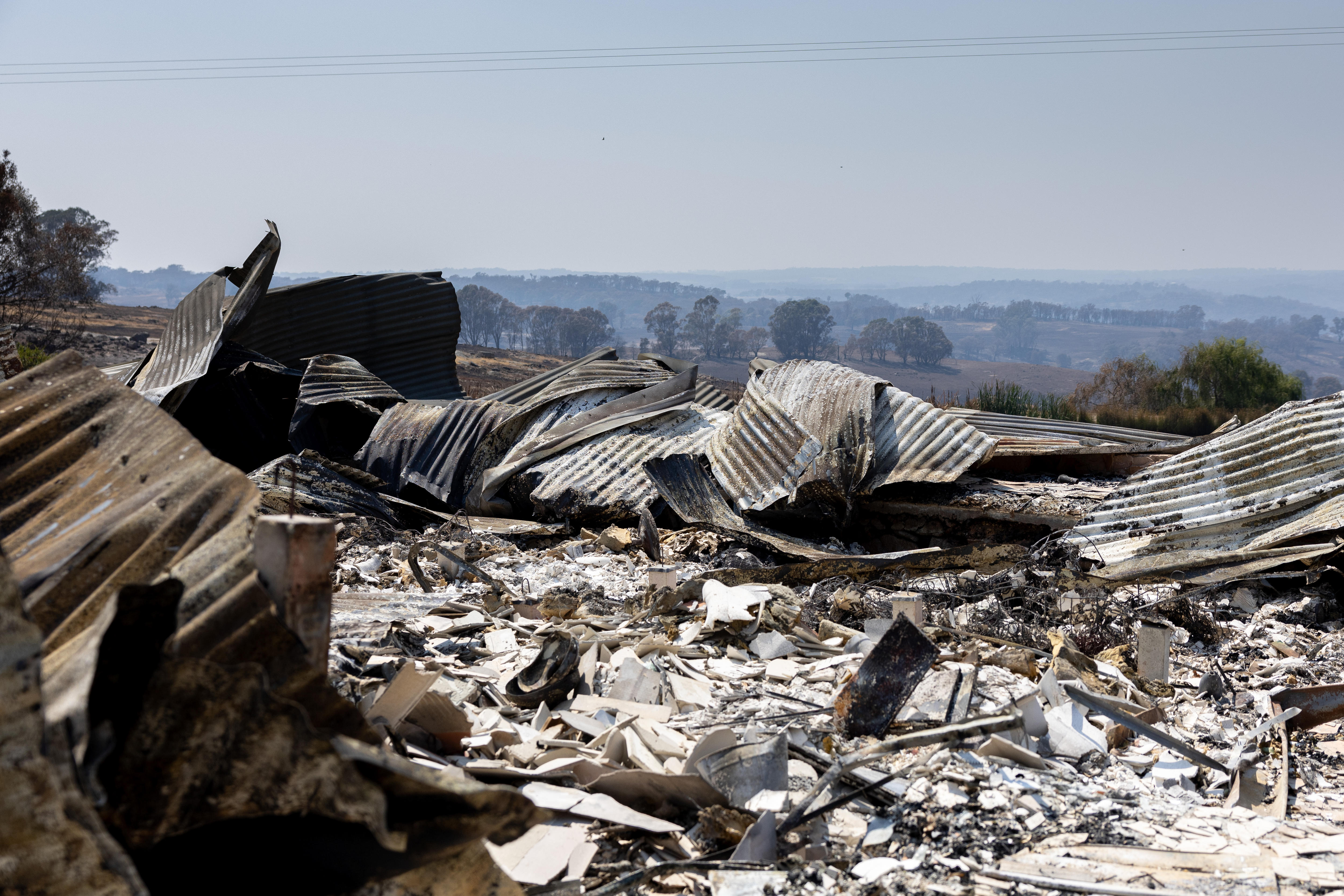 Restos de uma casa queimada, neblina no céu, colinas ao longe.