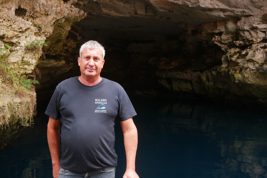 A man stands in front of the opening of an underwater cave