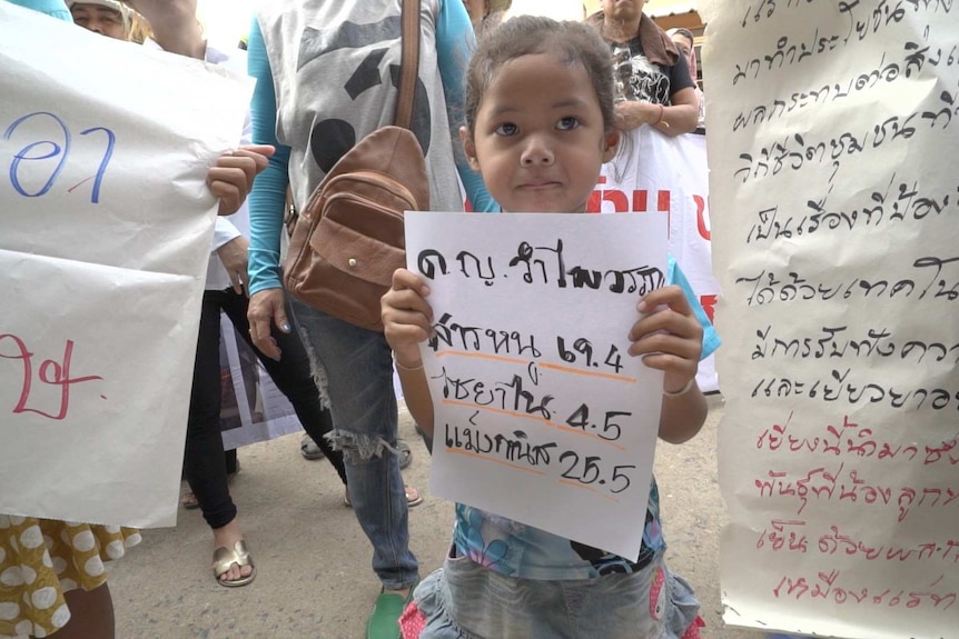 Girl holds sign with Thai writing at protest surrounded by other signs