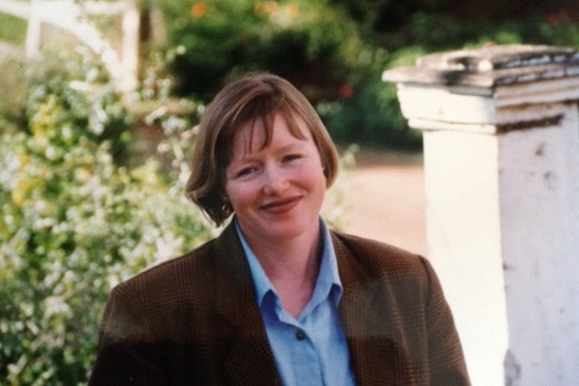 A woman with a bobbed haircut and brown jacket smiles at the camera.