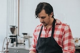 Male barista stands behind a wooden bar in a coffee shop for a story about mental ill health in the hospitality industry.