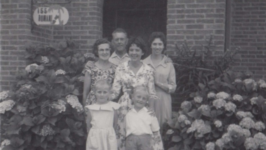 A group of people pose outside a suburban house in the 1950's. Black and white photo.