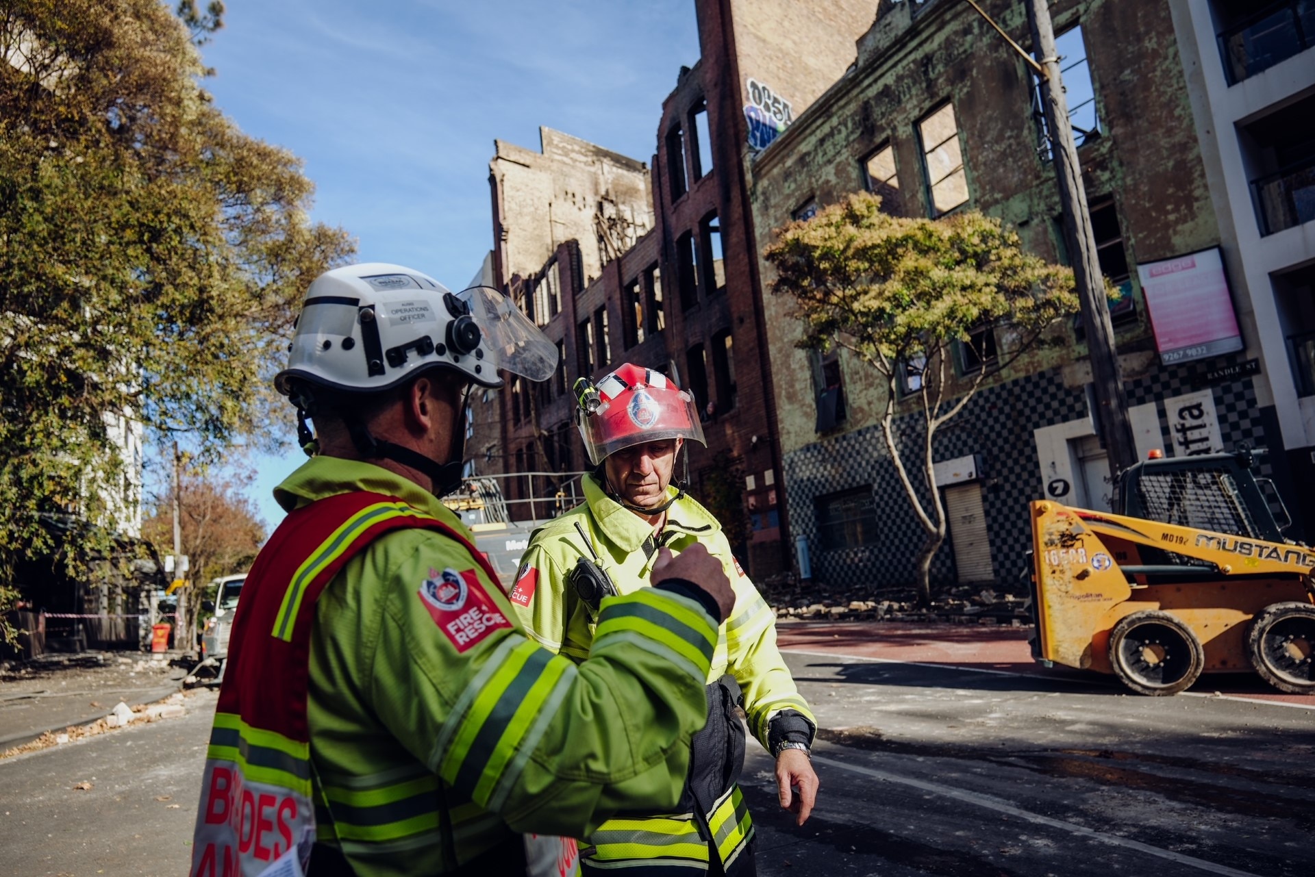 Two fire fighters on a street in front of a burnt out building 