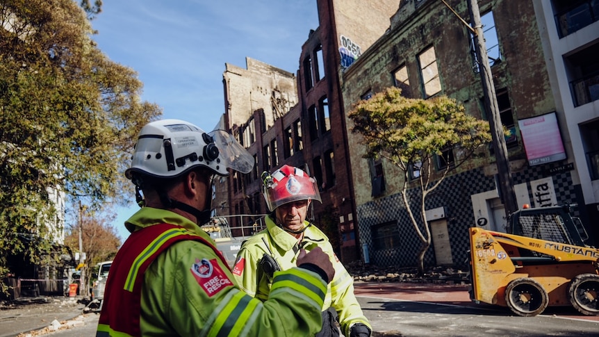Two fire fighters on a street in front of a burnt out building 