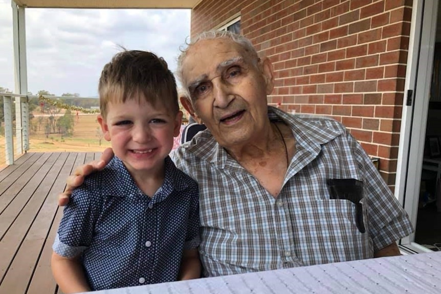 An old man hugs a young boy while sitting on the verandah of a house.