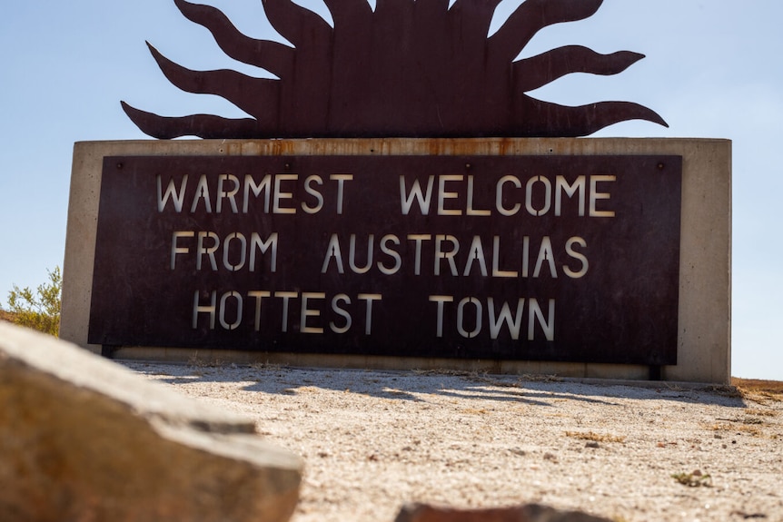 A wrought iron sign reading "warmest welcome from Australia's hottest town".