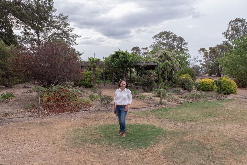 A woman stands on a small green patch of grass in a large garden