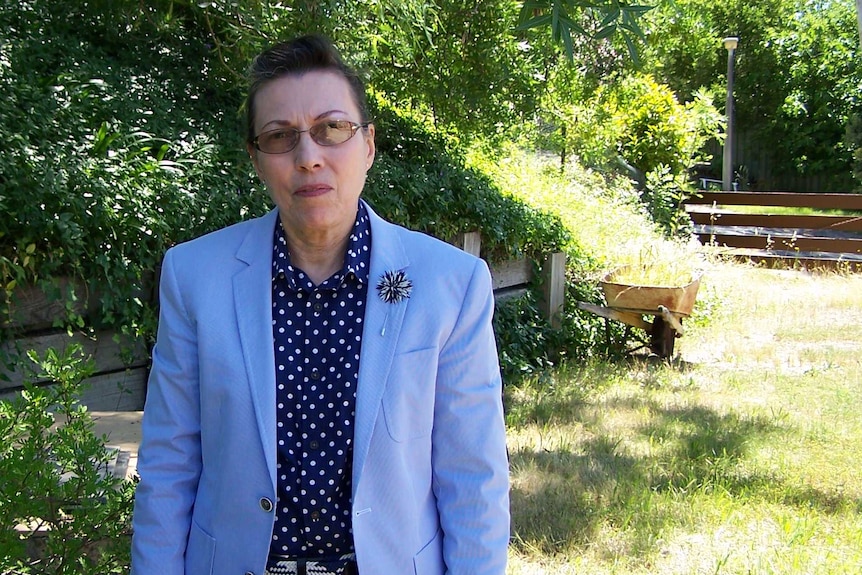 Curious Canberra questioner Shirley Llorens dressed in smart suit standing in a garden.