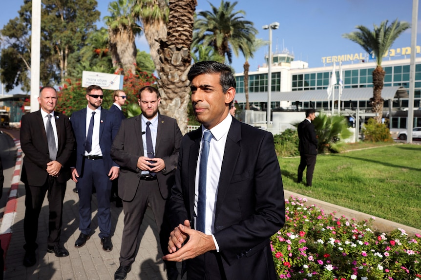 Rish Sunak stands with his hands clasped together dressed in a suit.