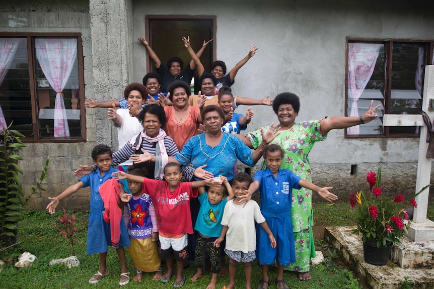 A group of women and children pose for a photo with their arms out at the community hall.