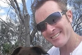 Dan Shearin smiles in a photo wearing sunglasses, holding a dog.