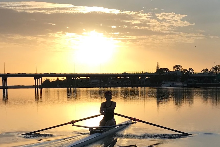 A woman rows on a river at dawn