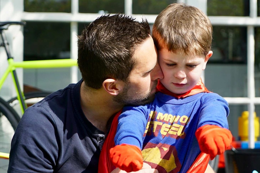 Leigh Chivers hugs his son Hugh, who is wearing a Superman costume.