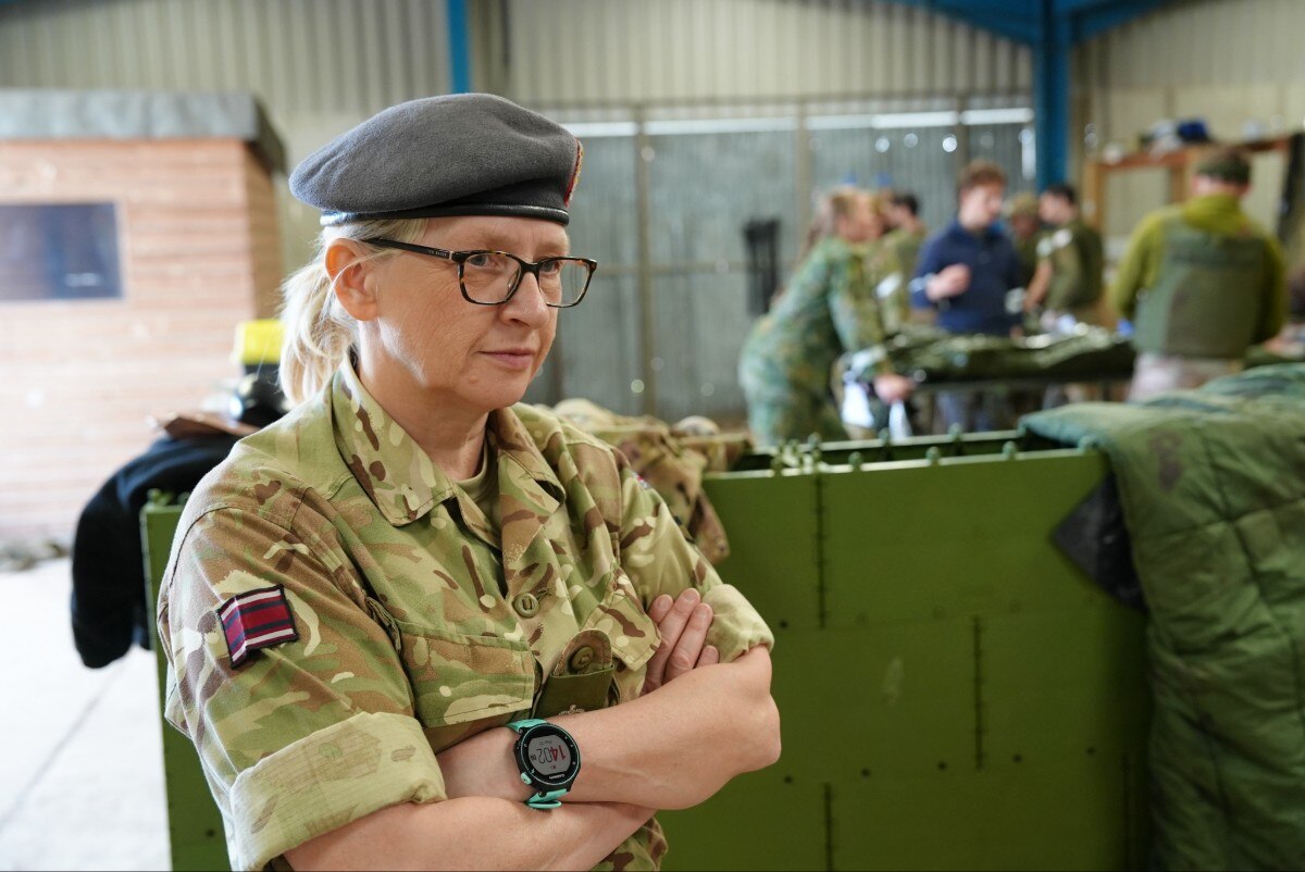A woman in uniform with her arms folded, looking on.
