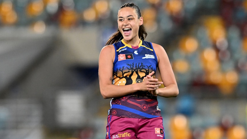 A Brisbane Lions AFLW player claps her hands as she celebrates a goal.