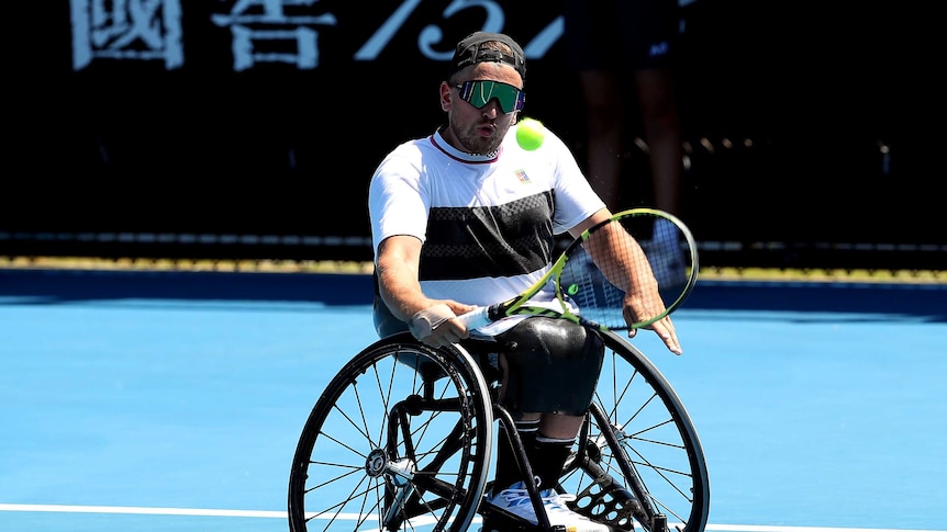 A man in a wheelchair hits a tennis ball with one hand