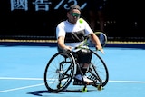 A man in a wheelchair hits a tennis ball with one hand
