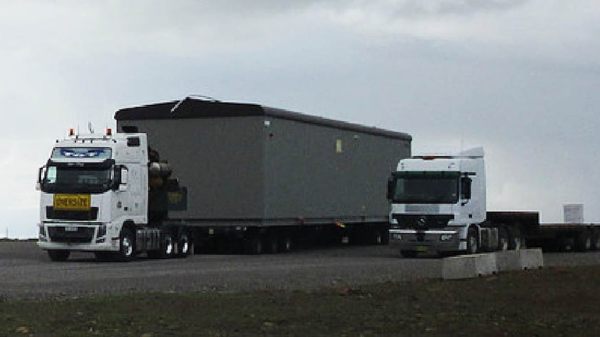 A truck carries a portable building, with a second truck alongside.