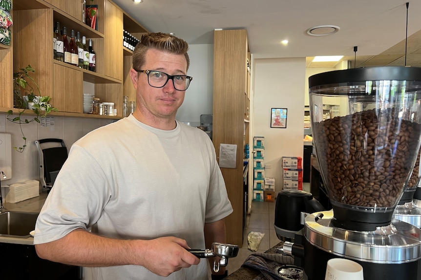 A slightly smiling man in glasses stands at a coffee machine.