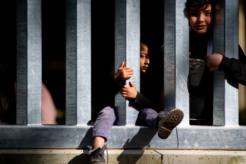 Two children sit on the wall, with legs and arms between the fence.