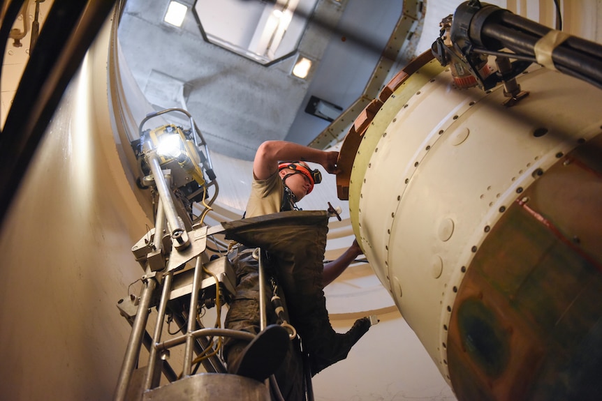 A techician atop a narrow platform works on an intercontinental ballistic missile that is sitting inside a launch silo.