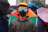 A Hong Kong protester stands with a hardhat, googles and other protection gear among umbrellas.