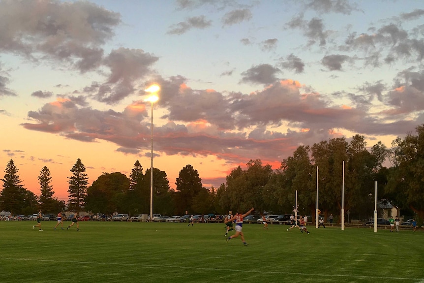 A country football match is played with the backdrop of a red-tinged sunset.