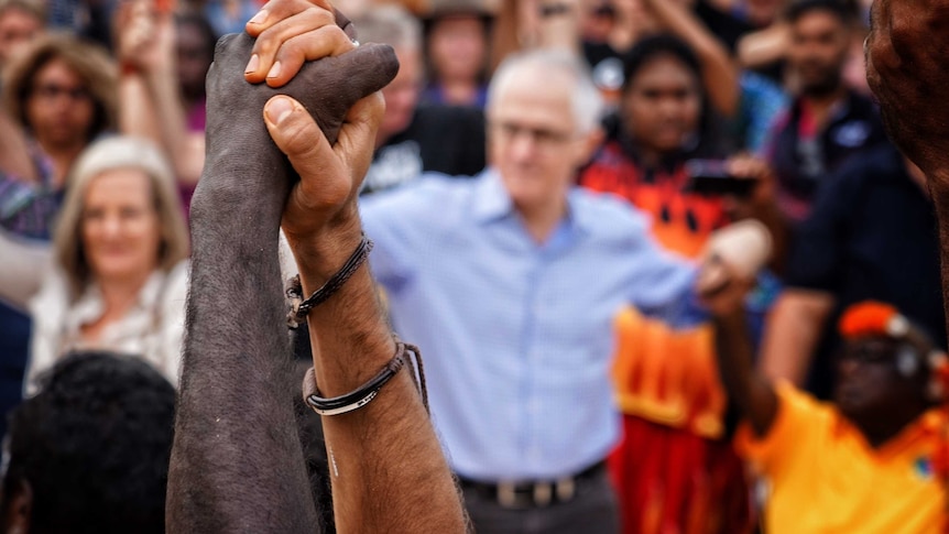 People hold hands at Garma festival with malcolm turnbull blurred in the background
