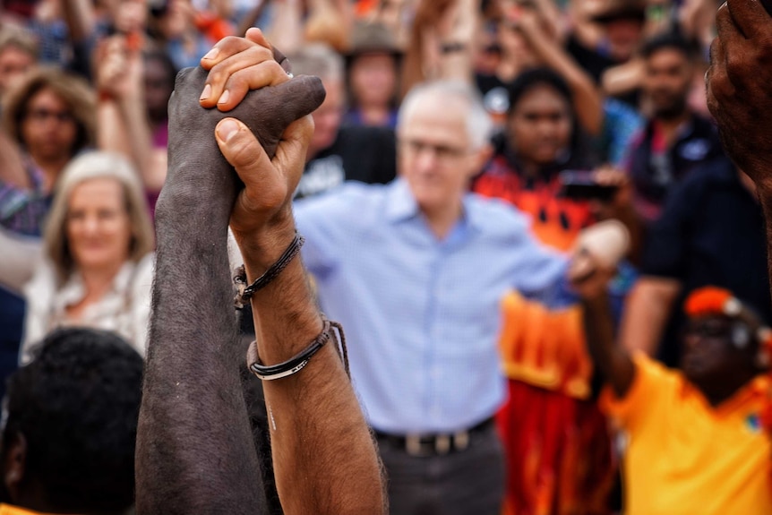 People hold hands at Garma festival with malcolm turnbull blurred in the background