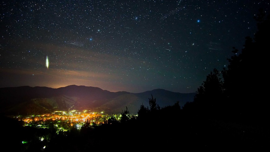 Meteors in the night sky above the lights of a small regional town.