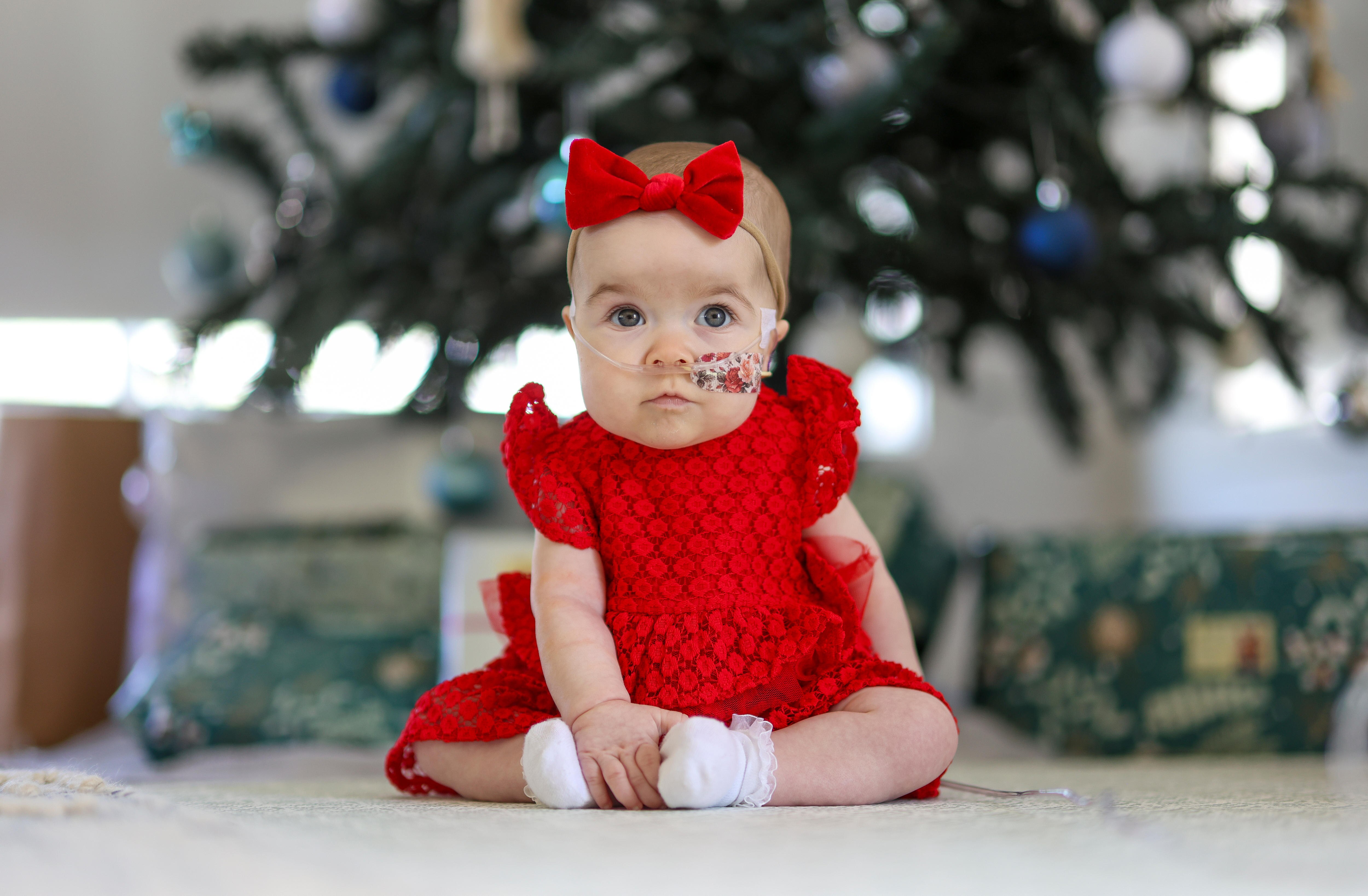 Elsie Cox in a red dress with a bow in her hair in front of a Christmas tree.