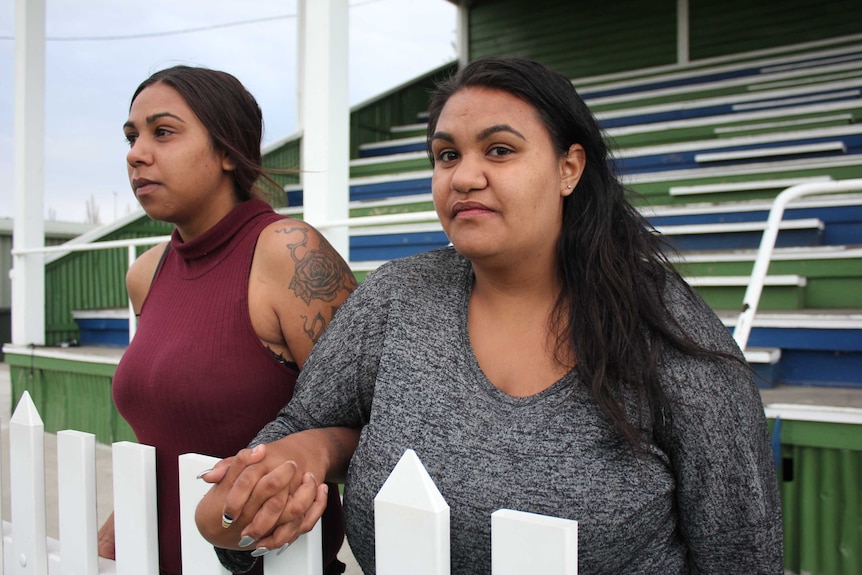 Sisters hold hand in front of a grandstand