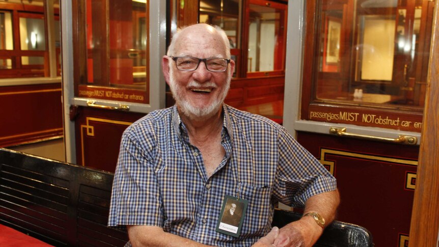 A man in a checked shirt with a white beard sitting in a bar.