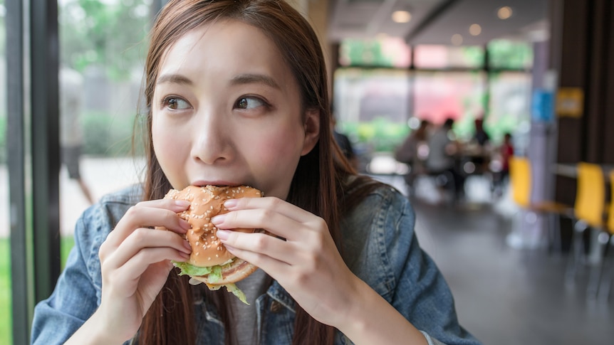 A woman smiles while eating a hamburger.
