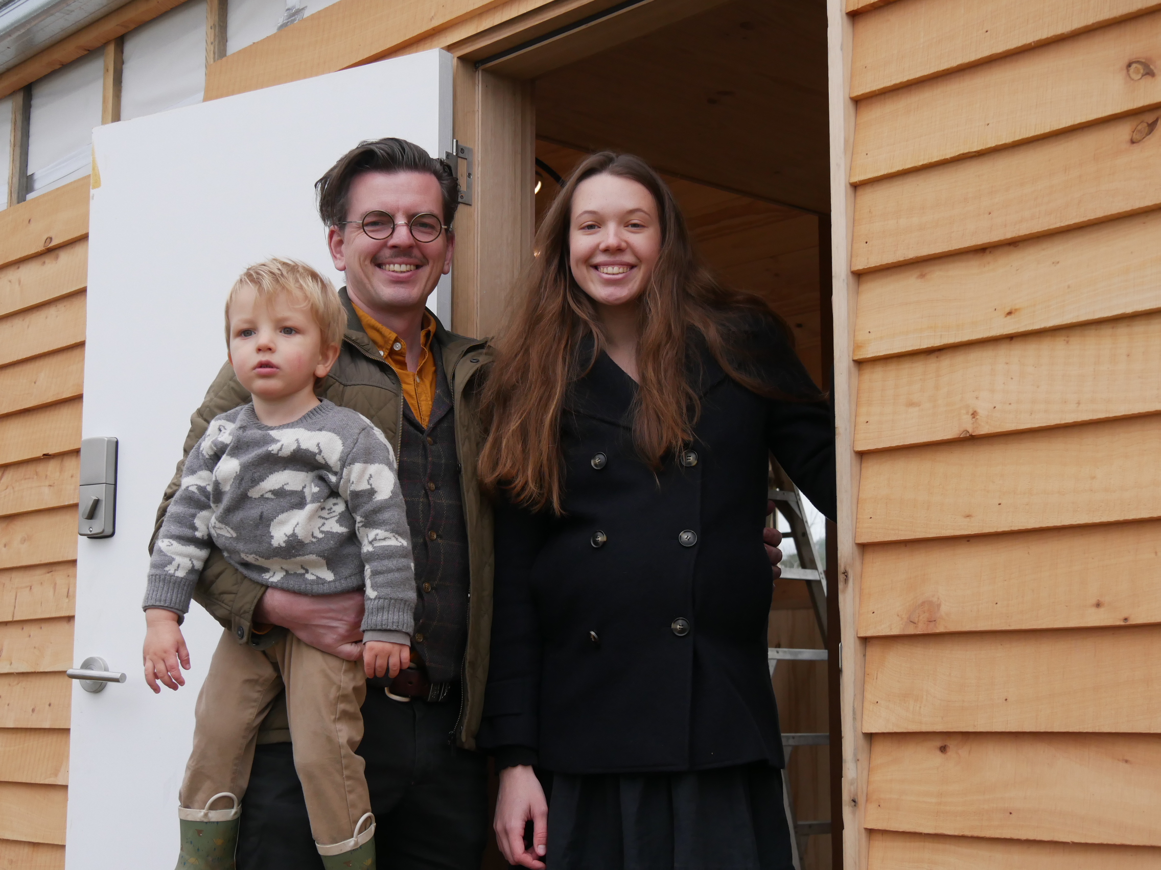 Family of three, a man holding a young boy and the mother next to them in the doorway of a new home.